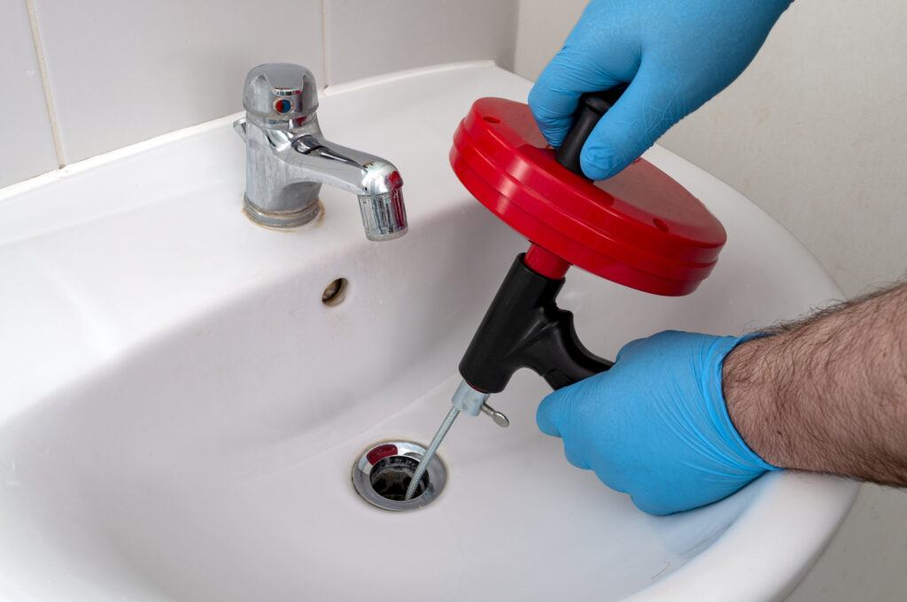 plumber snaking bathroom sink drain while wearing blue gloves