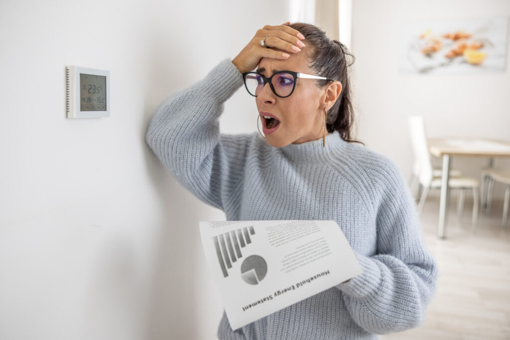 Woman cannot believe her own eyes the sum on her energy bill looking shocked at the thermostat on the wall next to her